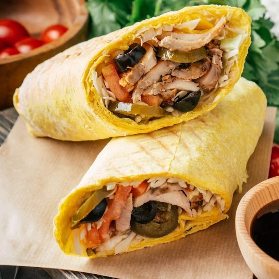 Two La Estrella Taqueria burritos, cut in half, revealing chicken, olives, and vegetables.