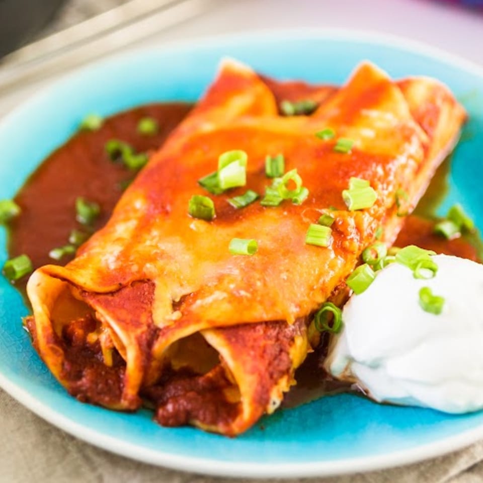 Two enchiladas covered in red sauce and green onions, with a dollop of sour cream.