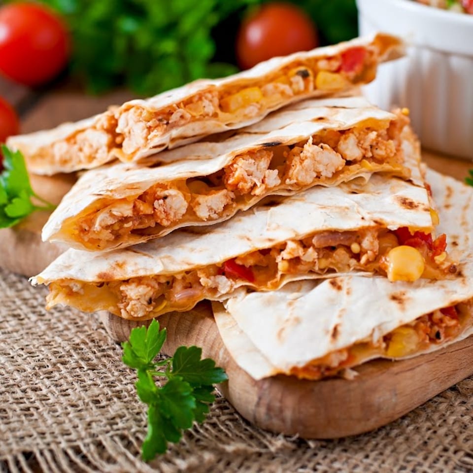 Chicken quesadillas with melted cheese, corn, and red peppers, served on a wooden board.