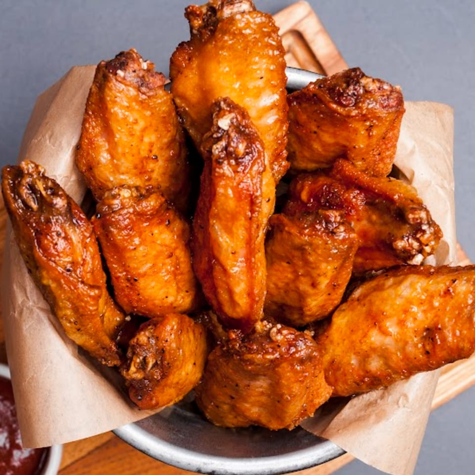 A metal bowl filled with crispy, golden-brown chicken wings, lined with brown parchment paper.